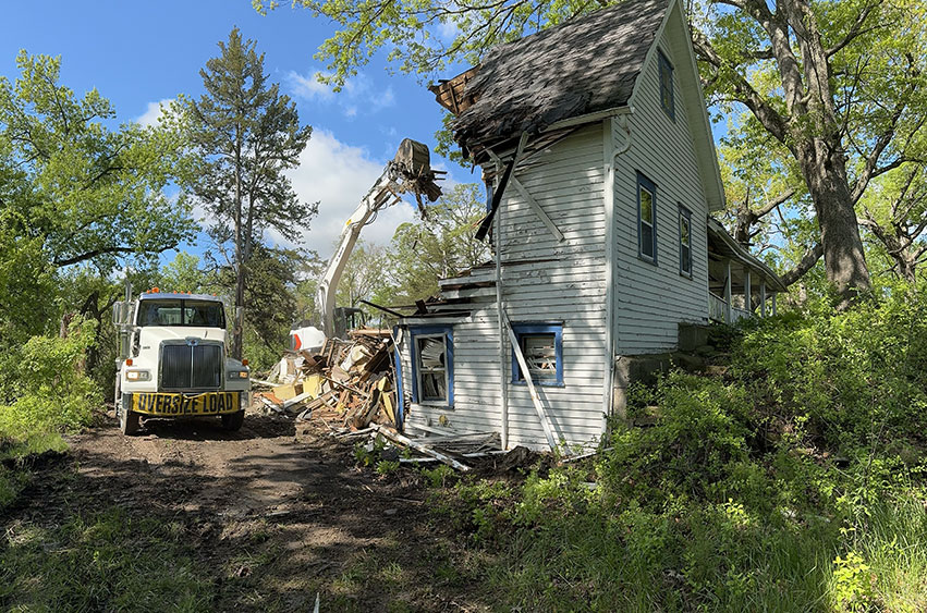 House demolition in progress, with an excavator removing the second story of an old home.