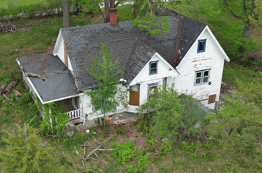 Abandoned Iowa home before demolition, surrounded by overgrown vegetation.