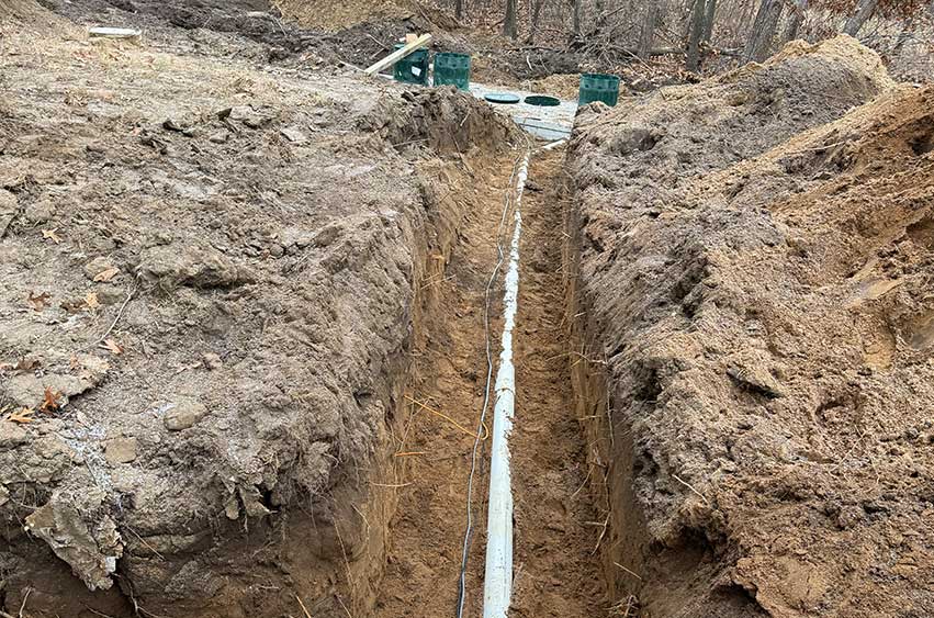 Long trench with a buried PVC sewer line running from the house to the septic tank.