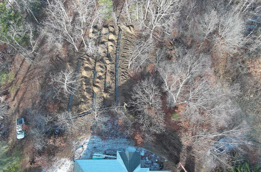 Aerial view of completed leach field trenches, backfilled and integrated into the wooded landscape.