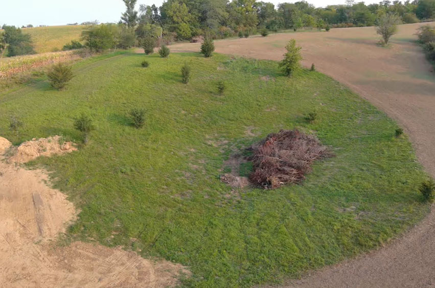 Aerial view of land before excavation, with a brush pile and grassy terrain in Iowa.