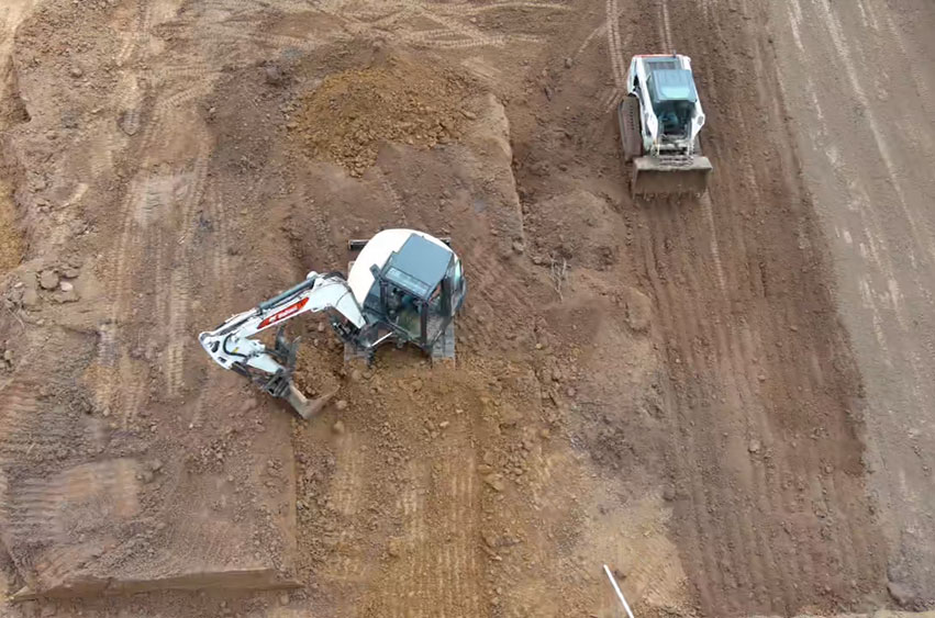 Excavator and skid loader working on leveling dirt for the shooting range foundation.